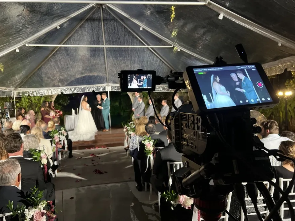 A Solfilms camera and monitors covering a bride and groom during an evening ceremony under a tent